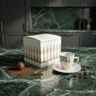 Espresso-Tasse „Stay Together – Gold“, limitierte Designer-Espressotasse mit stilisierter Figurenillustration von NONOS, hochwertige Porzellantasse mit Untertasse, Kaffee wird eingeschenkt, Detailaufnahme.